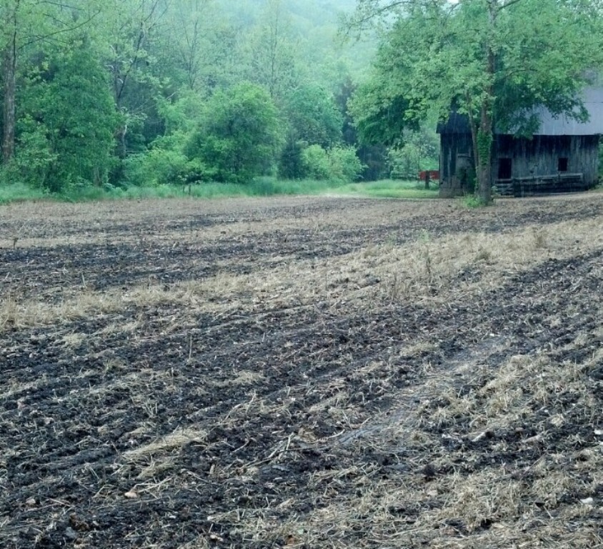 Open ground after planting with a barn in back ground
