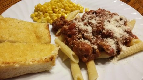 Plate of pasta with venison sauce, garlic bread and corn
